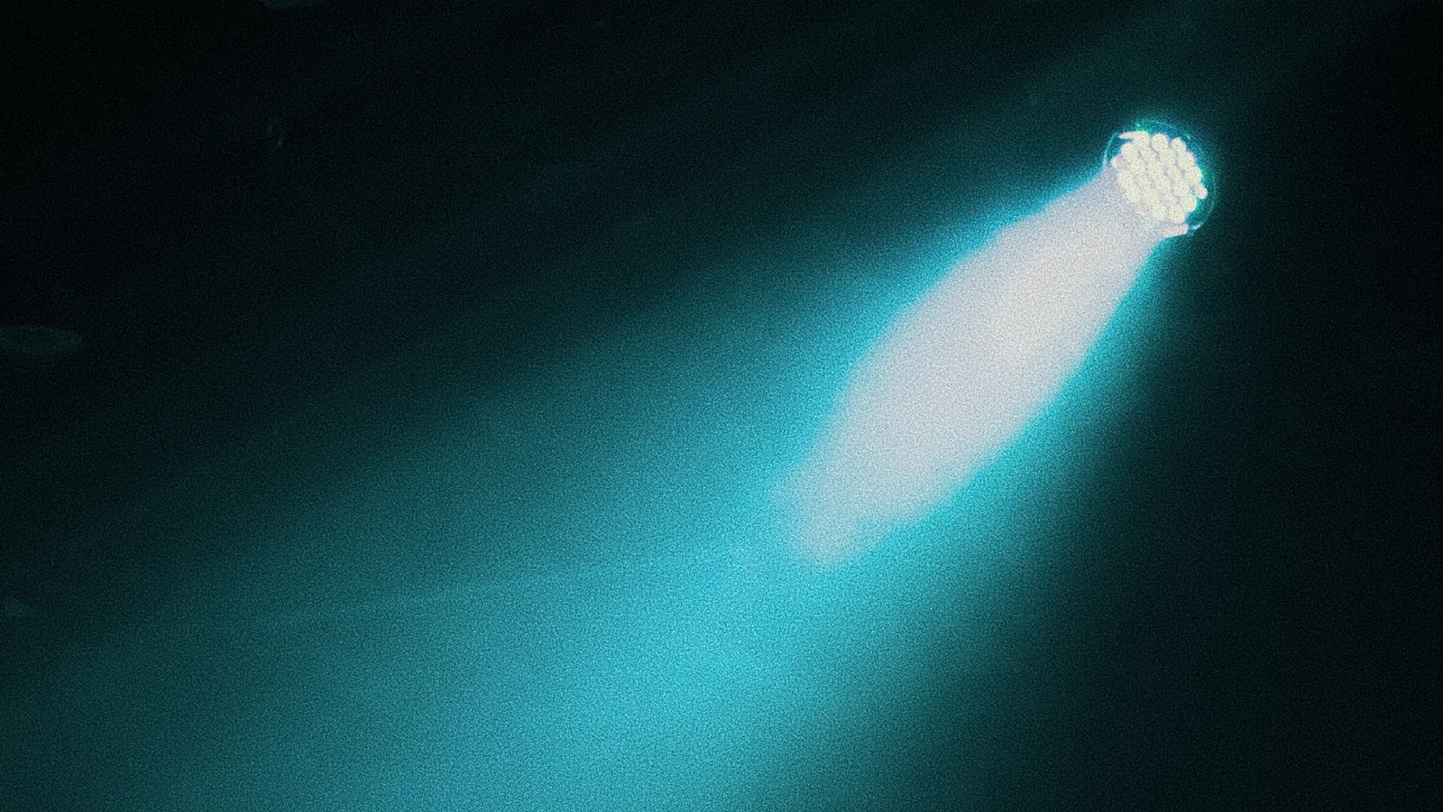 A teal spotlight beam cutting through a dark room